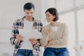 Serious couple study documents together, have serious looks, drink coffee, dressed in casual wear, plan their budget, pose in