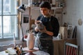 Serious craftswoman draws sketch on grey vase with thoughtful expression thinking about concept