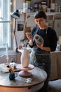 Serious craftswoman draws sketch on grey vase with thoughtful expression thinking about concept