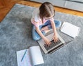 Serious cute little girl 8 years old in a striped T-shirt and jeans with glasses sits at home on a carpet in front of a laptop, Royalty Free Stock Photo