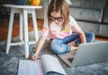 Serious cute little girl 8 years old in a striped T-shirt and jeans with glasses sits at home on a carpet in front of a laptop, Royalty Free Stock Photo