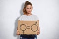 Serious cute young feminist with pony tail, holds plate with sign which demonstrates quality between sexes, dressed in casual t sh