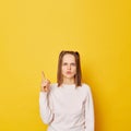 Serious displeased teenage girl in jumper with ponytails isolated over yellow background raised finger up has idea warning Royalty Free Stock Photo