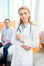 Serious doctor with stethoscope standing in chamber in hospital, with patient behind Royalty Free Stock Photo