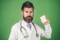 Serious doctor in white medical gown with stethoscope holds pills in hand. Pharmacy, medicine and healthcare concept. Royalty Free Stock Photo