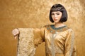 Serious Egyptian woman like Cleopatra with thumbs down gesture, on golden background Royalty Free Stock Photo