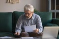 Serious elder grandpa holding papers using calculator counting loan payment