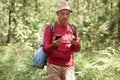 Serious enthusiastic man wandering in forest, holding compass and smartphone in his hands, choosing his travel route, being Royalty Free Stock Photo