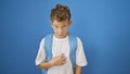 Serious-faced blond boy student standing, pointing at himself, isolated on a blue background