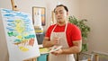 Serious-faced young asian artist, chinese male, holding his paintbrush and palette, standing in his in-house art studio