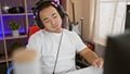 Serious-faced young chinese man streaming, immersed in virtual gaming world, playing video game, streaming at night indoors