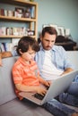 Serious father and son using laptop while sitting on sofa Royalty Free Stock Photo