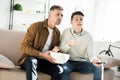 Serious father and teen son watching tv and holding bowl of popcorn