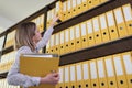 Serious female clerk takes folders from rack in archive Royalty Free Stock Photo