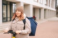 Serious female courier with big thermo backpack standing with electric scooter in city street looking at camera. Royalty Free Stock Photo