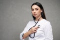 Serious female doctor listening heart beating with stethoscope.