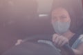 Serious female driver with protective face mask holding steering wheel of a car