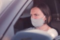 Serious female driver with protective face mask holding steering wheel of a car