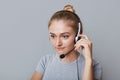 Serious female helpline operator uses headphones for her work, being focused on something, isolated over grey background. Business Royalty Free Stock Photo