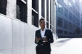 Serious female student thinking, holding and using phone, african american business woman with cup of hot drink walking on break Royalty Free Stock Photo