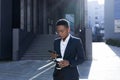 Serious female student thinking, holding and using phone, african american business woman with cup of hot drink walking on break Royalty Free Stock Photo