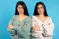 Serious female twins in casual clothes on a blue background, with crossed hands look at the camera