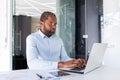 Serious and focused african american businessman in shirt working inside office with laptop, mature investor financier