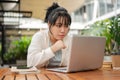 A serious, focused Asian woman is working remotely at an outdoor space, reading email on her laptop Royalty Free Stock Photo