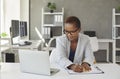 Young black business woman sitting at office desk, looking at laptop screen and taking notes Royalty Free Stock Photo