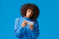 Serious focused cute african-american girl playing interesting game on smartphone turning mobile phone, holding Royalty Free Stock Photo