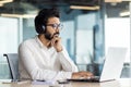 Serious and focused Indian young man working in the office on a laptop. He is wearing headphones and is sitting at his Royalty Free Stock Photo