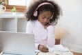 Serious focused little African girl in headphones makes schoolwork