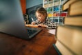 Serious focused primary child school girl doing homework writing notes in paper notebook sitting at table with laptop. Royalty Free Stock Photo