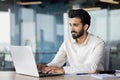 A serious and focused young Indian man is working on a laptop in the office. He sits at his desk and types on the Royalty Free Stock Photo