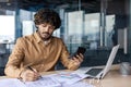 Serious and focused young Indian man working in office at desk with documents. Processes data and accounts, uses a Royalty Free Stock Photo