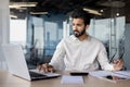 Serious and focused young Indian man working in office at desk, typing on keyboard, processing data and searching for Royalty Free Stock Photo