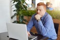 A serious freckled red head student wearing stylish checked shirt and watch sitting in cosy cafe keeping his hands on keyboard of