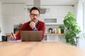 Serious freelancer writing notes in notepad while doing research over laptop at desk in home office Royalty Free Stock Photo