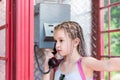 A serious girl with afro-braids makes a phone call in an old English telephone booth. Generational contrast Royalty Free Stock Photo