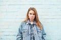 Serious girl in a denim jacket stands against a blue wall and looks at the camera. Hipster girl in the casual clothing poses Royalty Free Stock Photo