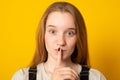 Serious girl dressed casually holding finger at her lips asking not to make noise or hold tongue. Royalty Free Stock Photo