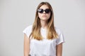 Serious girl dressed in a white t-shirt and sun glasses is on a white background in the studio