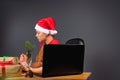A serious girl elf writes a wish list and receives letters online on a laptop at a table with gifts. Gray background Royalty Free Stock Photo