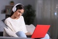 Serious girl with headphones checking laptop content in the night