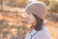 A serious girl in a knitted hat stands against a background and a coat against the backdrop of an autumn pale park landscape