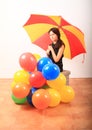 Serious girl with red and yellow umbrella behind inflating balloons