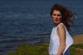 Serious girl in white dress with a stern gaze outdoors on river shore, deep blue water on background. Royalty Free Stock Photo