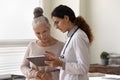 Serious GP doctor showing tablet screen to old female patient Royalty Free Stock Photo