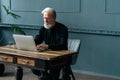 Serious gray-haired mature journalist male working on laptop, article creation sitting at wooden table at home office. Royalty Free Stock Photo