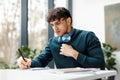 Serious guy doing his home assigment looking attentively in copybook and writing info, sitting in university audience